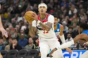 Washington Wizards player in a white jersey holding the ball mid-air, preparing for a shot while defended by Milwaukee Bucks players.