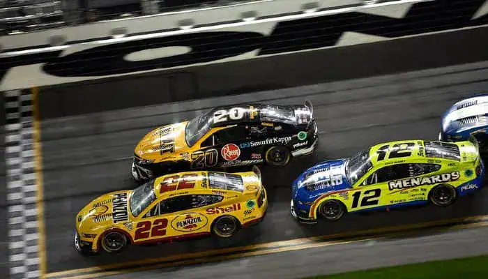 NASCAR race with three cars competing side by side at high speed on the track.