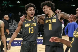 Two Baylor basketball players, smile and celebrate together on the court after a game.