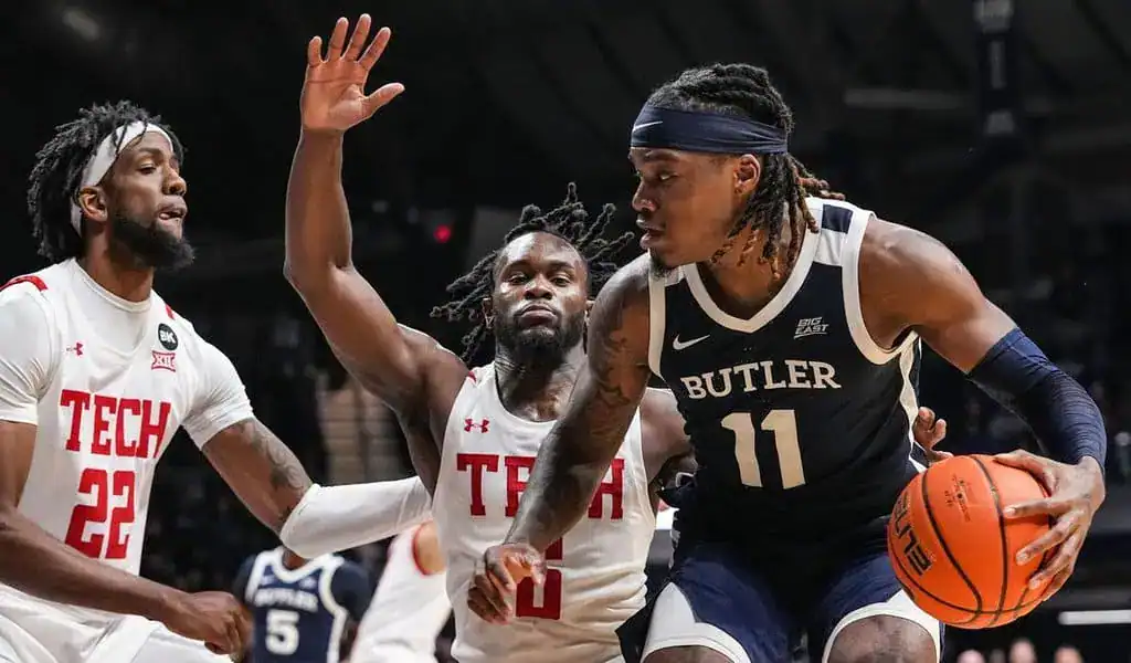 Butler player with number 11 tries to push past two Texas Tech defenders while holding the ball.