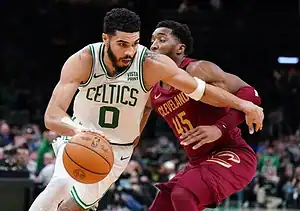 Boston Celtics player drives to the basket while being tightly defended by a Cleveland Cavaliers player.