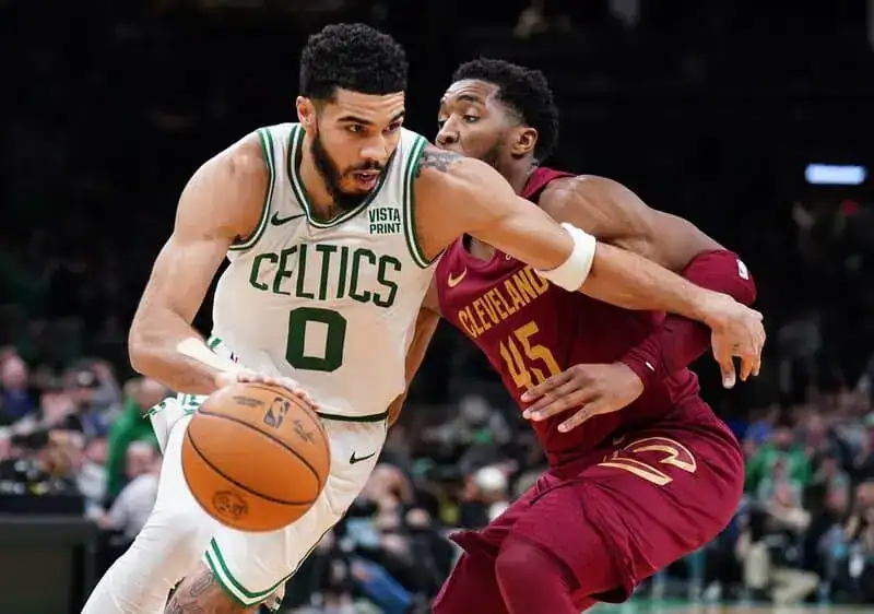 Boston Celtics player drives to the basket while being tightly defended by a Cleveland Cavaliers player.