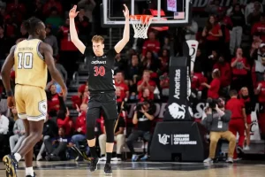 A Cincinnati basketball player raises both arms in celebration after a play.