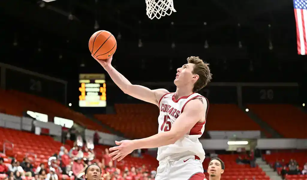 Washington State Cougars player going up for a layup during a college basketball game.