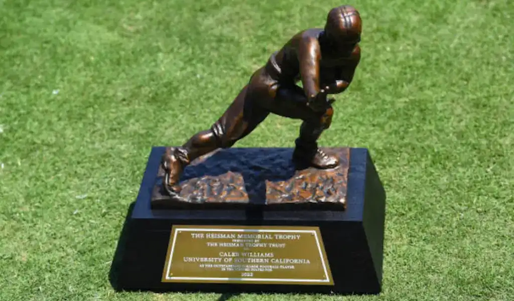 Trofeo Heisman otorgado al mejor jugador de fútbol universitario, exhibido en un campo de césped con una placa grabada.
