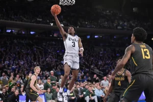 A Duke basketball player goes up for a layup while being challenged by multiple defenders.