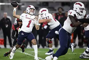 Fresno State quarterback in a white uniform winds up to throw a pass while under pressure.
