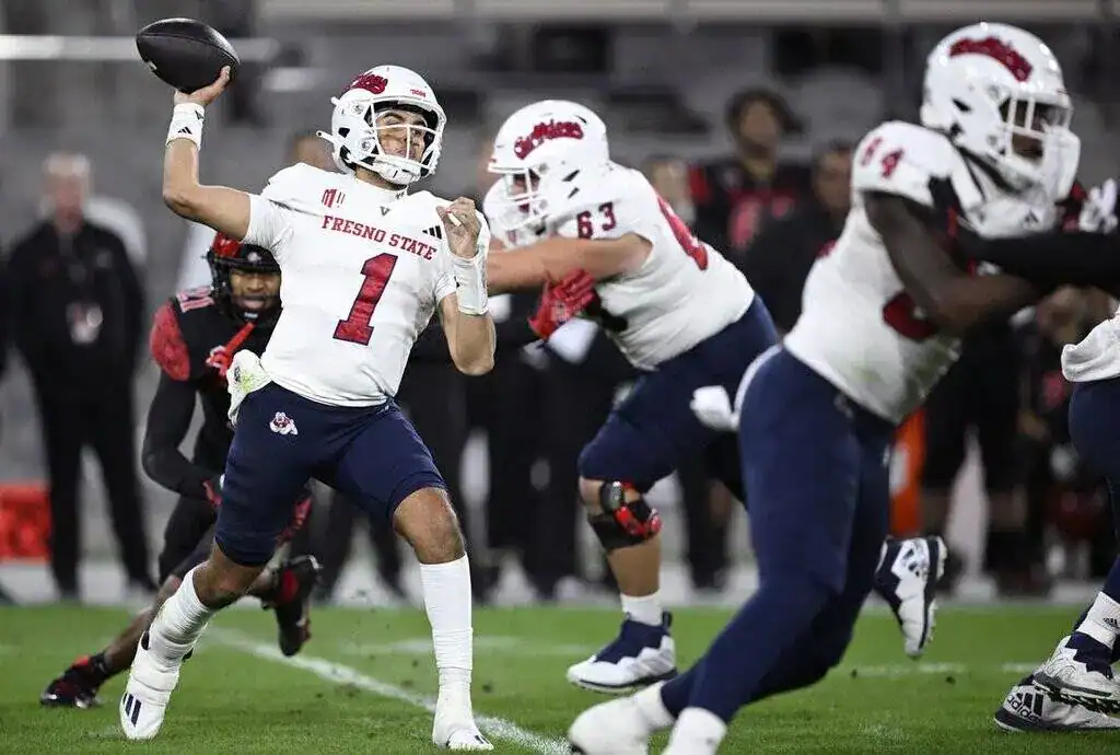 Fresno State quarterback in a white uniform winds up to throw a pass while under pressure.
