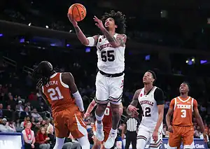Louisville Cardinals basketball player drives to the basket against Texas Longhorns defender.