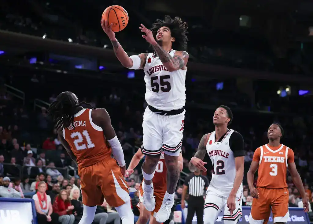 Louisville Cardinals basketball player drives to the basket against Texas Longhorns defender.