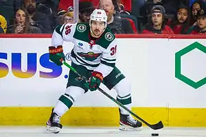 Minnesota Wild player in a white jersey handles the puck during an NHL game.