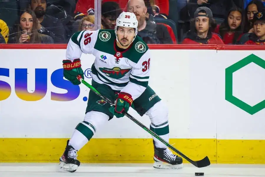 Minnesota Wild player in a white jersey handles the puck during an NHL game.