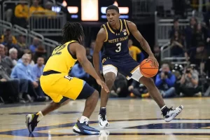 A Notre Dame basketball player dribbles the ball while sizing up a defender from Marquette.