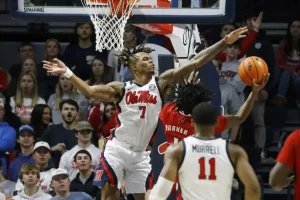 This is an action-packed basketball image showing Ole Miss player attempting to block a shot from an opposing player in red.