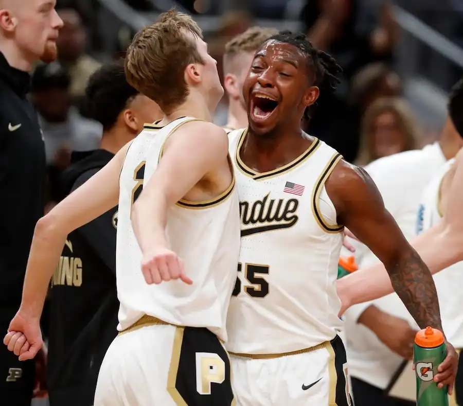 Two Purdue basketball players celebrate on the sideline with excitement during a game.