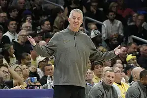 Purdue basketball coach stands courtside with arms out, gesturing during a game.