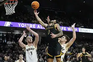Northwestern player attempts a layup against Purdue defenders during a college basketball game.