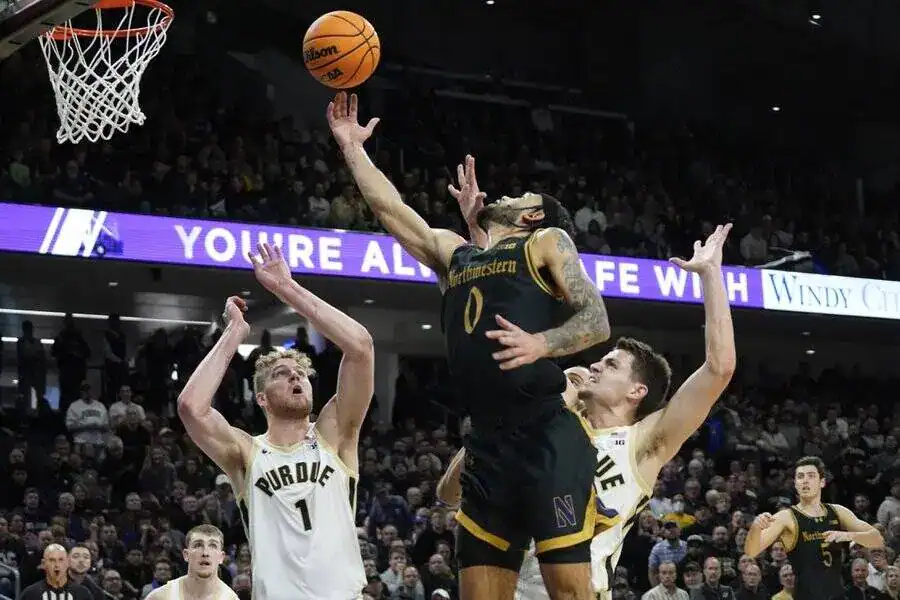 Northwestern player attempts a layup against Purdue defenders during a college basketball game.