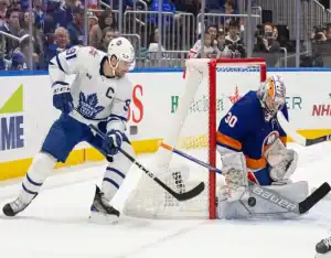 Toronto Maple Leafs forward controls the puck behind the net while New York Islanders goalie defends
