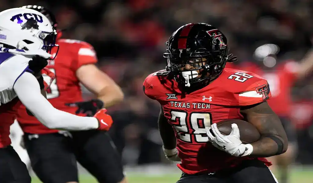 Texas Tech Red Raiders running back carries the ball while defended by a TCU player during a college football game.
