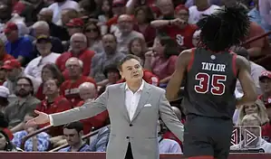 St. John’s Red Storm coach talks to a player during a college basketball game as fans watch from the stands.