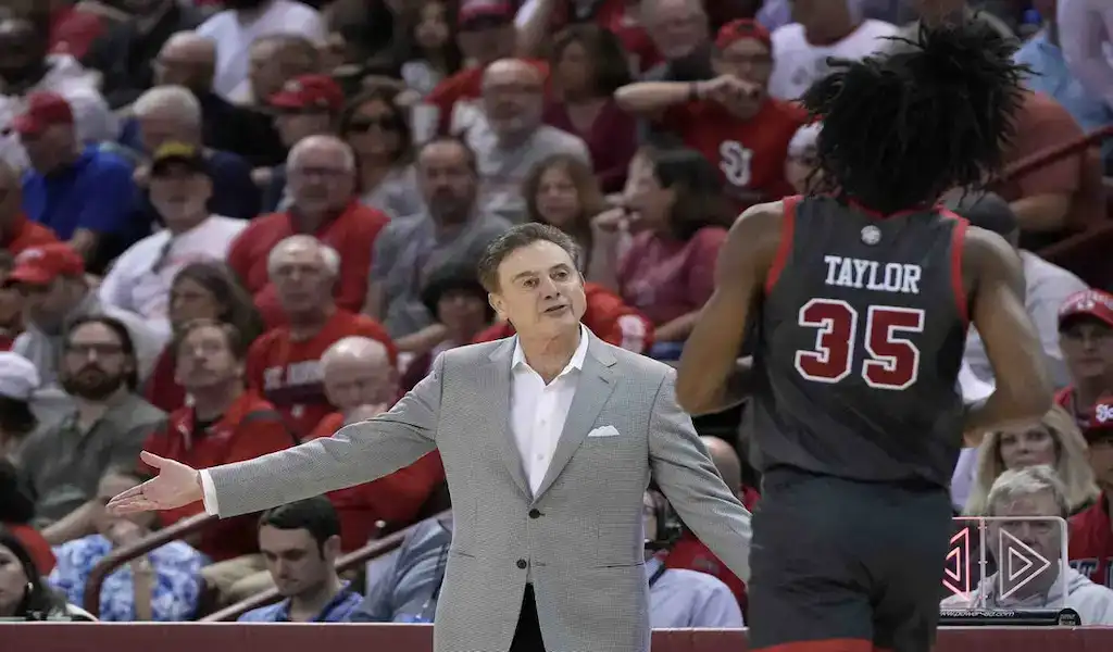 St. John’s Red Storm coach talks to a player during a college basketball game as fans watch from the stands.