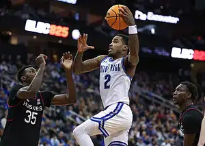 Seton Hall player in a white jersey drives to the hoop for a layup against defenders.