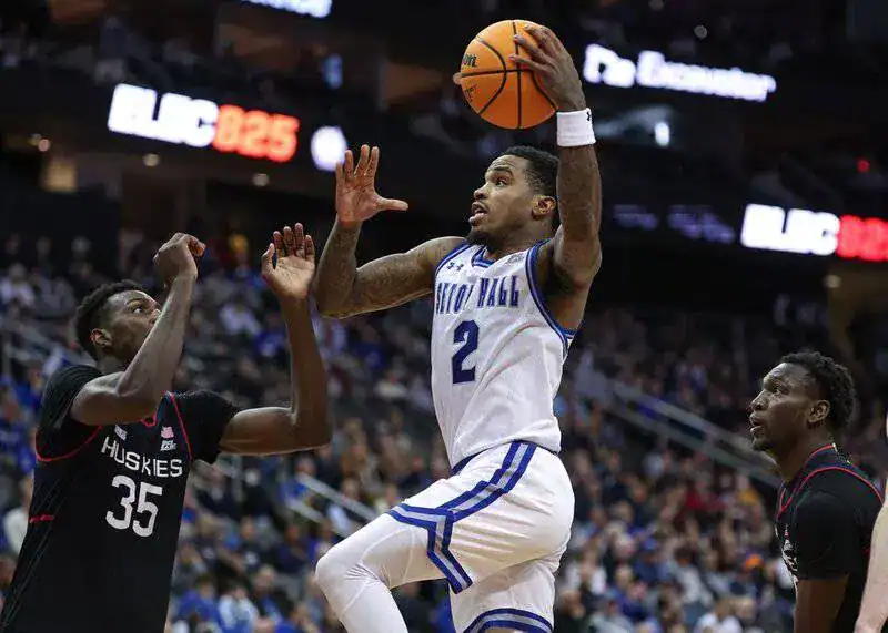 Seton Hall player in a white jersey drives to the hoop for a layup against defenders.