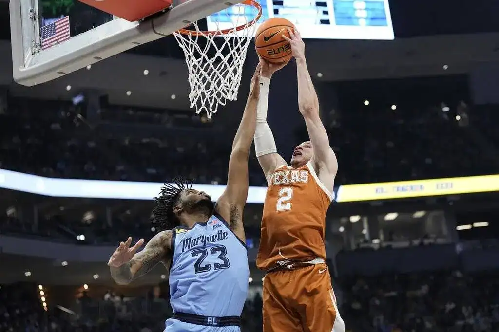 Texas Longhorns basketball player dunking while defended by a Marquette player under the basket.