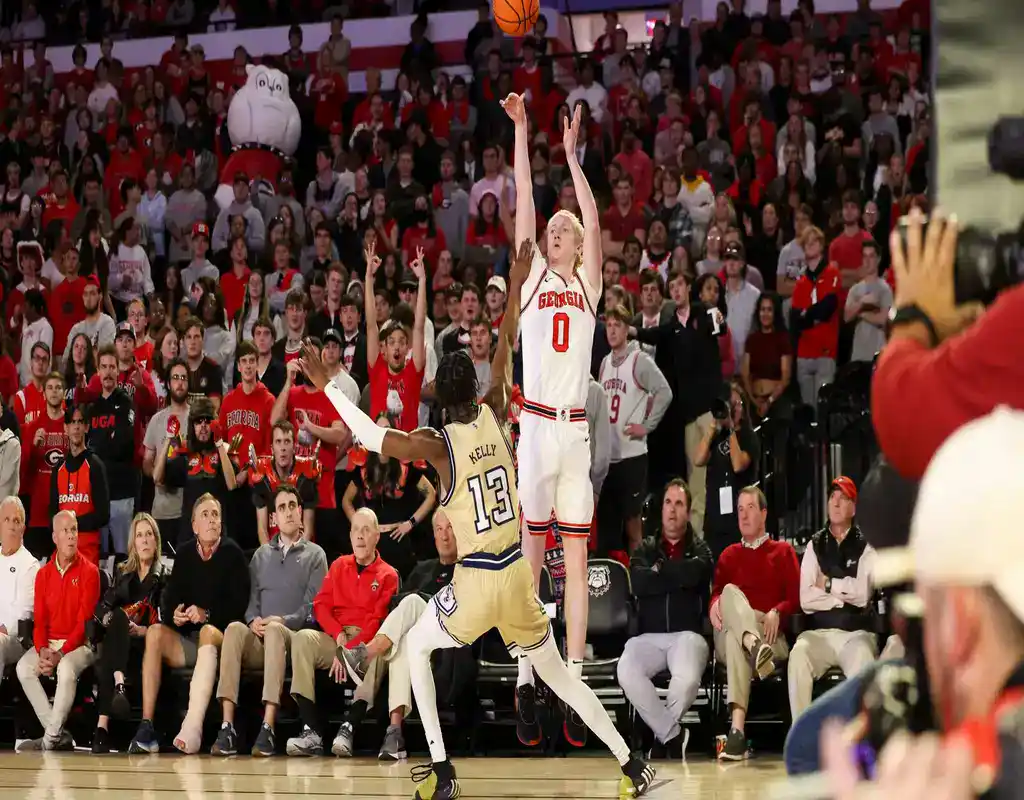 NCAAB 1 Georgia Bulldogs player #0 leaping for a jump shot over Alabama A&M defender #13 in front of the crowd