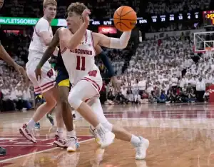 “Wisconsin Badgers #11 driving past a Michigan State Spartans defender in a packed basketball arena.”