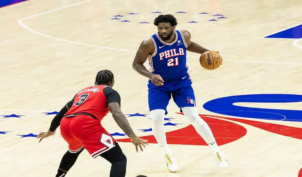 Philadelphia 76ers player dribbles the ball while being defended by a Chicago Bulls opponent during an NBA game.