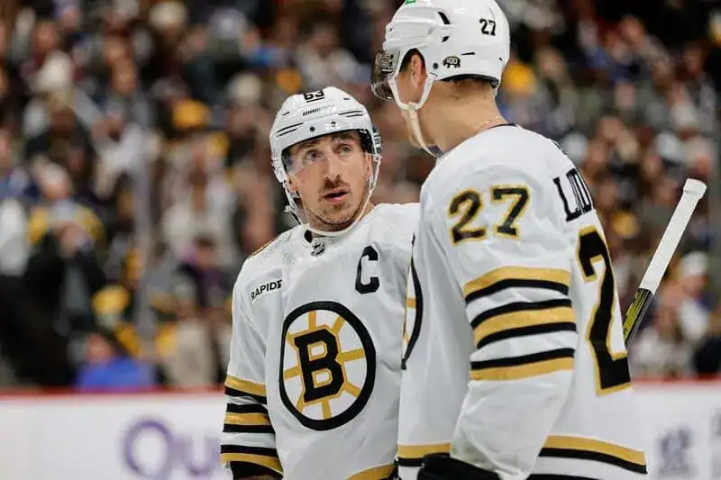 NHL 8 Two Boston Bruins players in white jerseys chat on the ice during a stoppage in play.