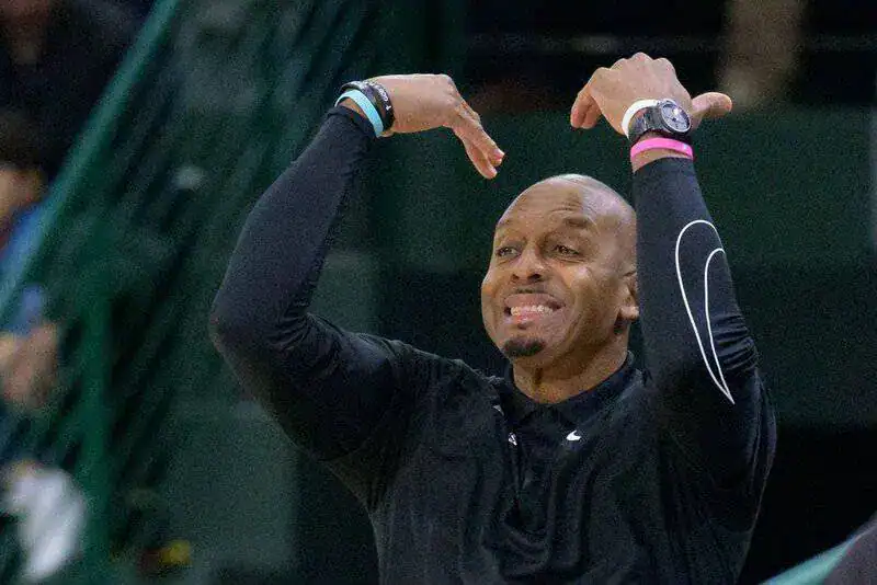 Basketball coach in black raises both arms, signaling while shouting instructions to his team.