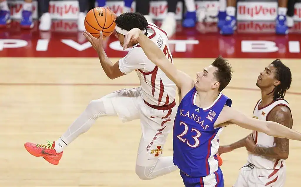 A basketball player leaps in mid-air, preparing to shoot, while another player from the opposing team attempts to block him.
