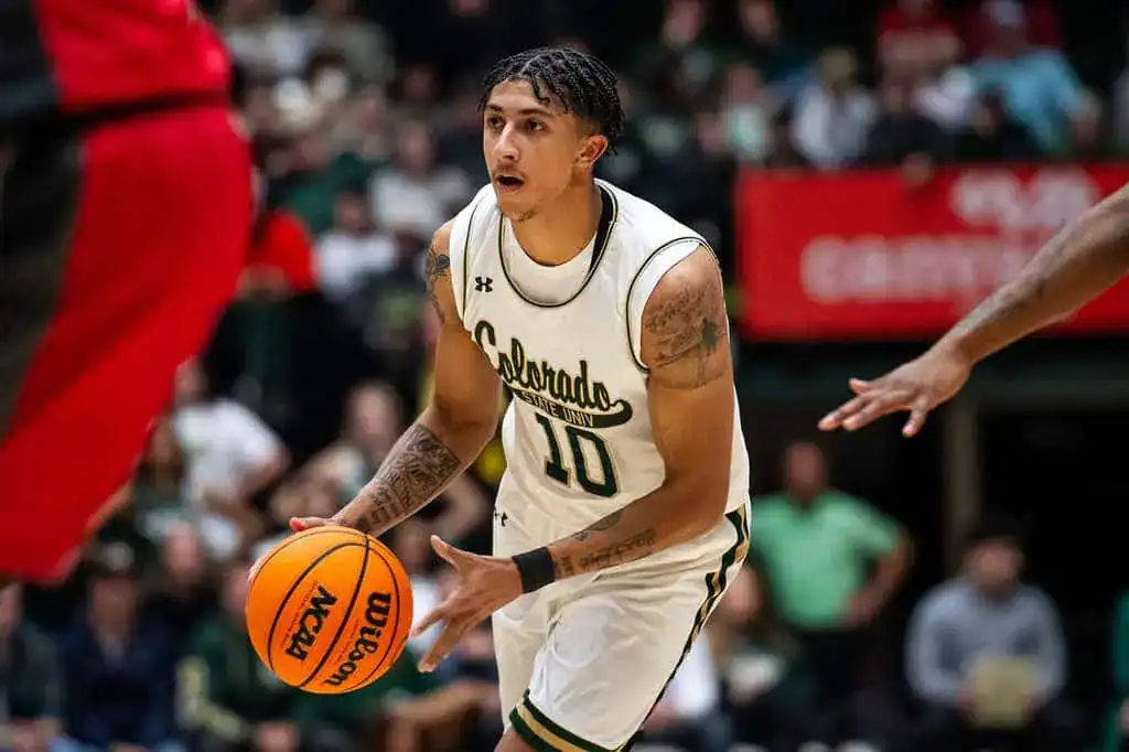 Colorado State University basketball player dribbling the ball in a white and green uniform during an NCAA game.