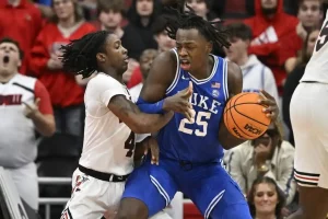 A Duke basketball player battles for position while holding the ball tightly against a Louisville defender.