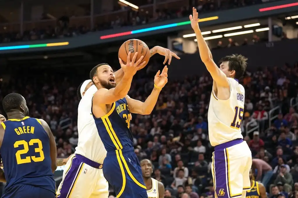 Warriors player drives to the basket for a layup while being defended by Lakers player.