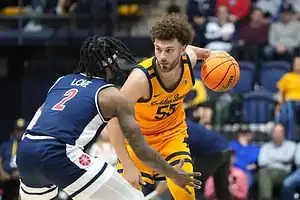 A basketball player in a yellow jersey dribbles the ball, evading a player in a navy and red uniform during an intense game.