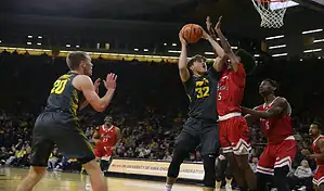 Iowa Hawkeyes player going up for a contested shot against Rutgers Scarlet Knights defenders during a college basketball game.