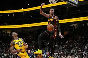 A basketball player from the Atlanta Hawks soars midair for a dunk while an Indiana Pacers defender looks on.