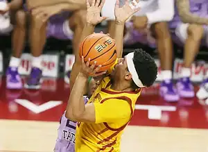 Iowa State player in a yellow and red uniform goes up for a contested shot near the basket.