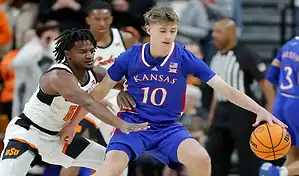 Kansas Jayhawks guard dribbles past West Virginia Mountaineers defender during NCAA basketball game.