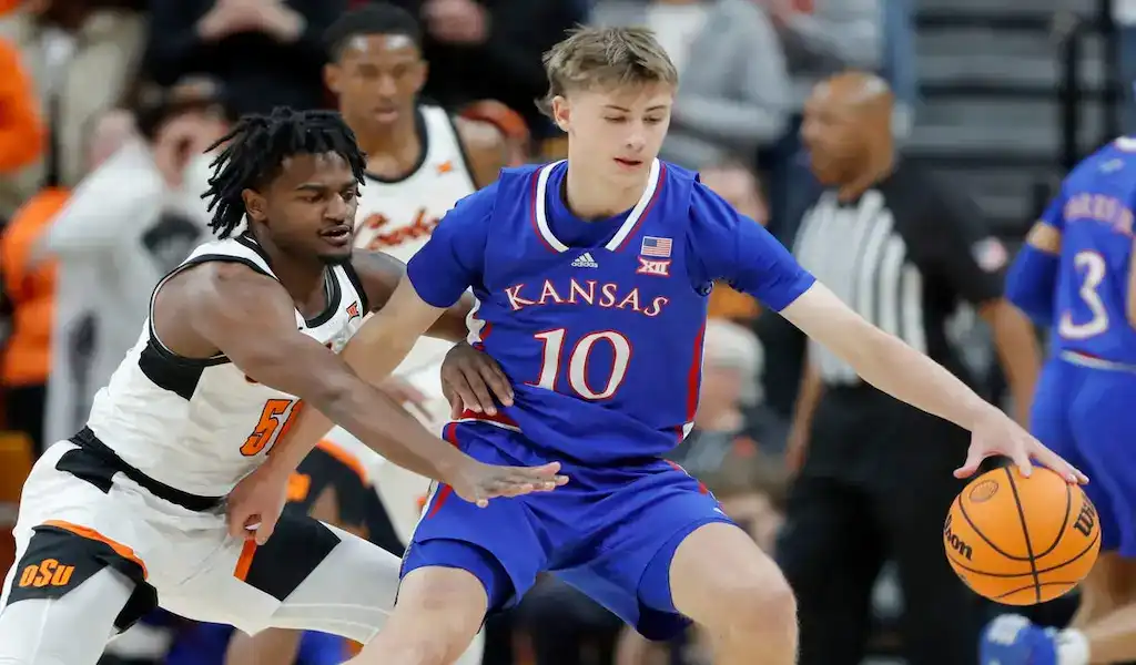 Kansas Jayhawks guard dribbles past West Virginia Mountaineers defender during NCAA basketball game.