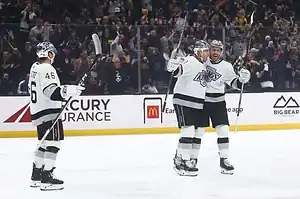 Los Angeles Kings players celebrating a goal on the ice as fans cheer in the background.