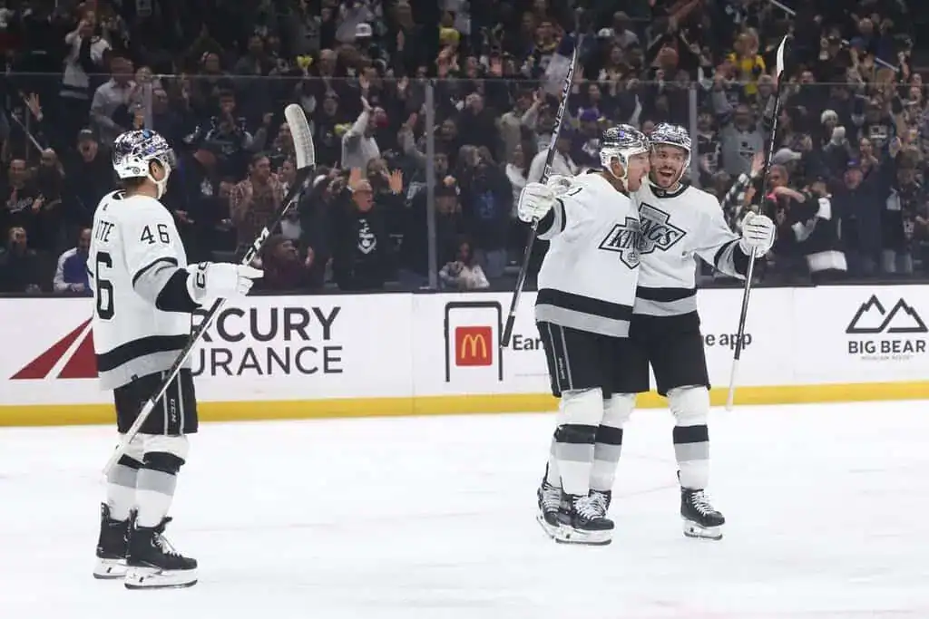 Los Angeles Kings players celebrating a goal on the ice as fans cheer in the background.