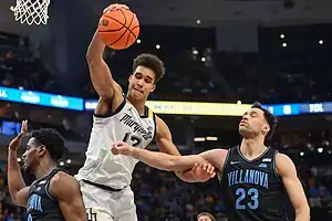 Marquette basketball player goes up for a dunk while a Villanova defender attempts to contest the play during an NCAA game.