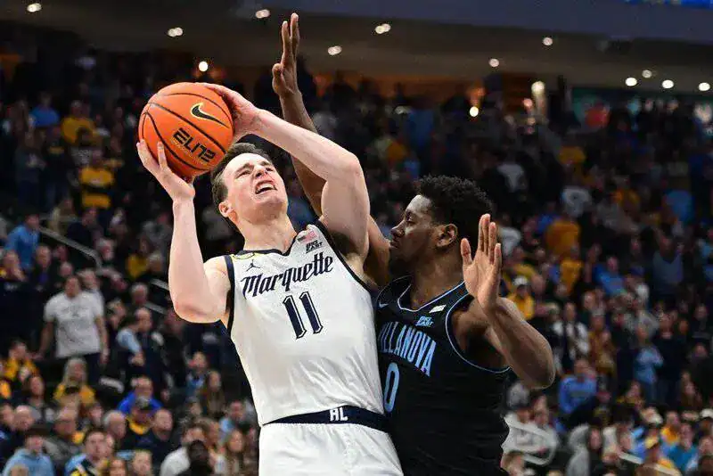 Marquette basketball player drives toward the basket, attempting a contested shot against Villanova defender.