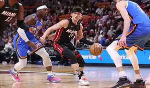 Miami Heat player dribbles past Oklahoma City Thunder defenders during a basketball game.
