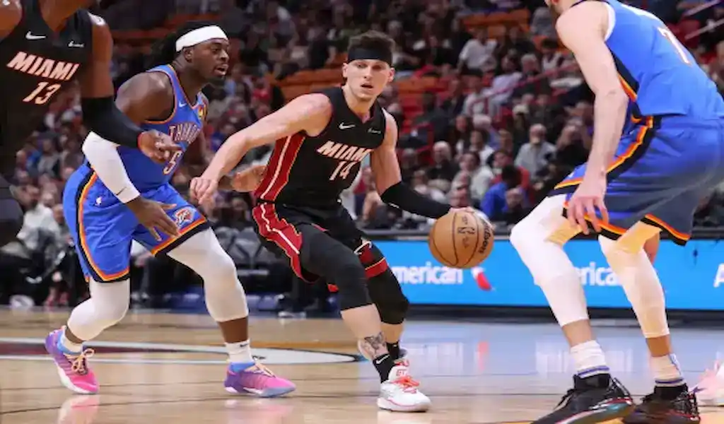 Miami Heat player dribbles past Oklahoma City Thunder defenders during a basketball game.